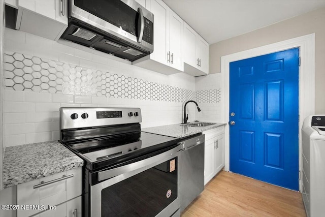 kitchen with sink, appliances with stainless steel finishes, light stone counters, white cabinets, and washer / clothes dryer