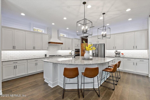 kitchen featuring pendant lighting, an island with sink, white cabinetry, custom exhaust hood, and stainless steel fridge with ice dispenser