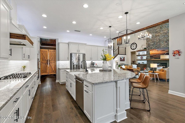 kitchen featuring an island with sink, white cabinetry, sink, hanging light fixtures, and stainless steel appliances