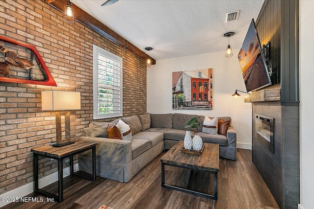 living room with a tile fireplace, brick wall, dark wood-type flooring, and a textured ceiling