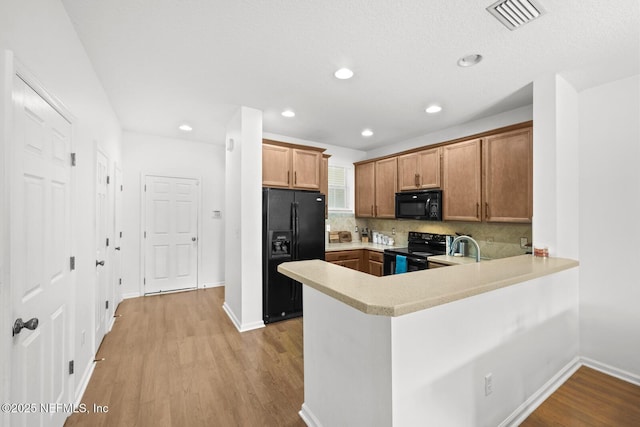 kitchen with a peninsula, visible vents, light countertops, brown cabinets, and black appliances