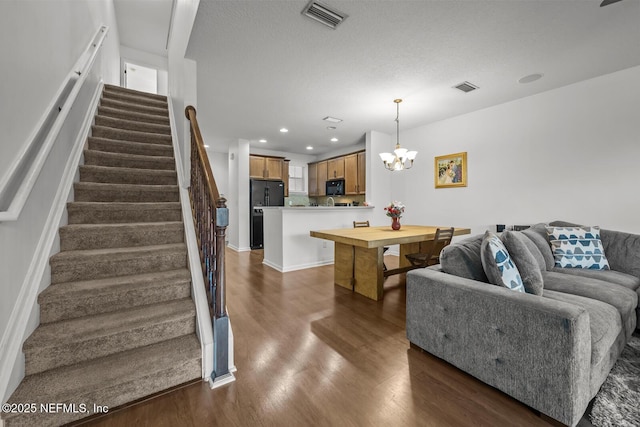 living area with stairs, dark wood finished floors, visible vents, and an inviting chandelier