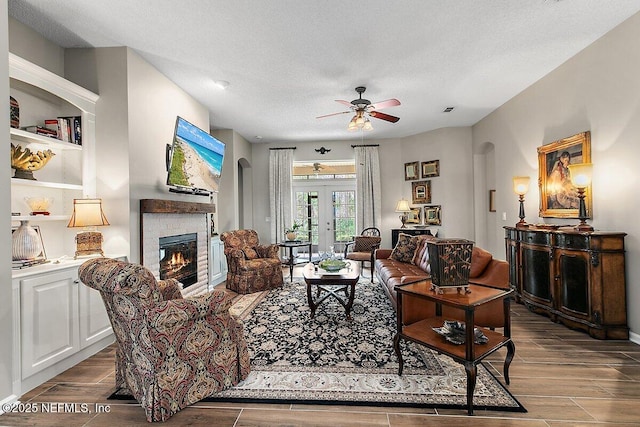 living room featuring ceiling fan, a stone fireplace, french doors, and a textured ceiling