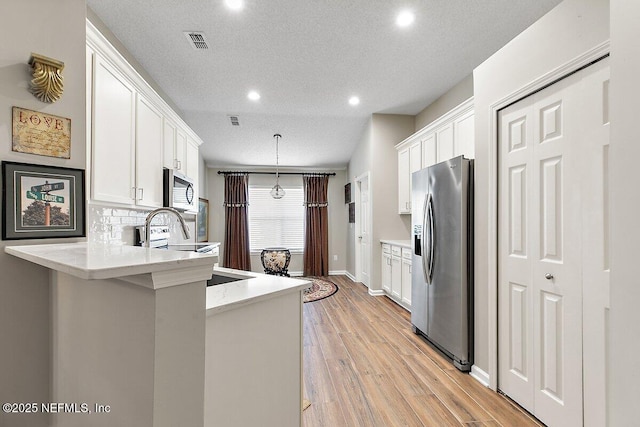 kitchen with pendant lighting, light hardwood / wood-style flooring, appliances with stainless steel finishes, white cabinetry, and kitchen peninsula