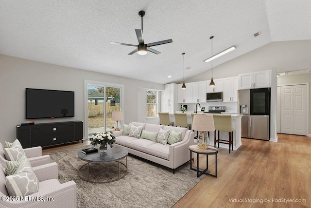 living room with lofted ceiling, sink, ceiling fan, light hardwood / wood-style floors, and a textured ceiling