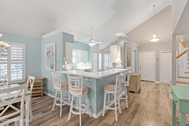 kitchen with hanging light fixtures, vaulted ceiling, light hardwood / wood-style flooring, and kitchen peninsula