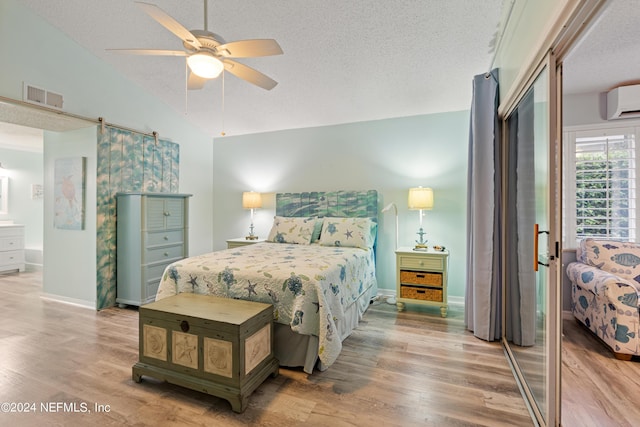 bedroom with vaulted ceiling, wood-type flooring, a wall mounted air conditioner, and a textured ceiling