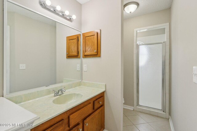 bathroom with tile patterned floors, vanity, a shower with shower door, and a textured ceiling