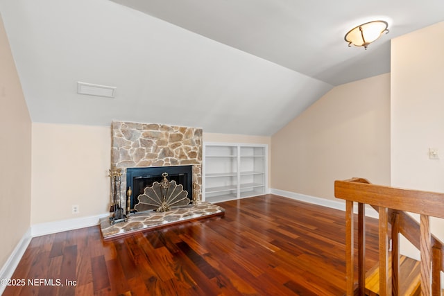 living room featuring lofted ceiling, hardwood / wood-style floors, a stone fireplace, and built in shelves