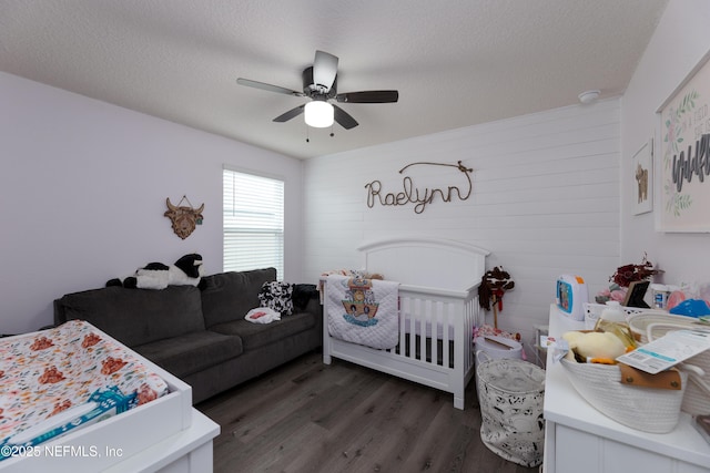 bedroom with dark hardwood / wood-style flooring, ceiling fan, a crib, and a textured ceiling