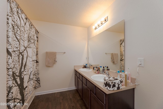 bathroom with a textured ceiling, wood finished floors, a sink, and baseboards