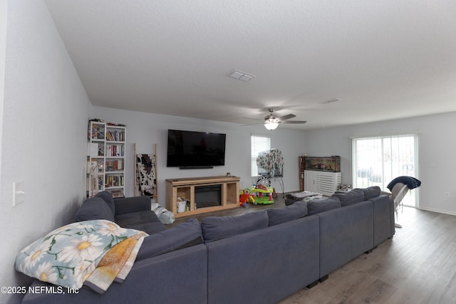 living room with a wealth of natural light, visible vents, a textured ceiling, and wood finished floors