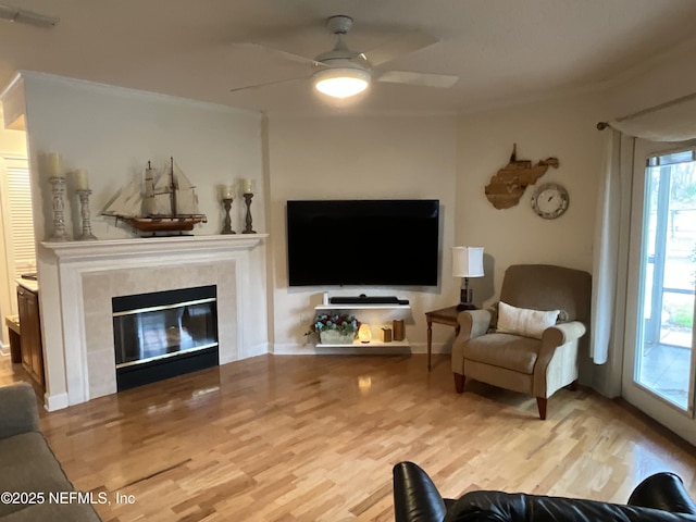 living room featuring a tiled fireplace, wood-type flooring, and crown molding