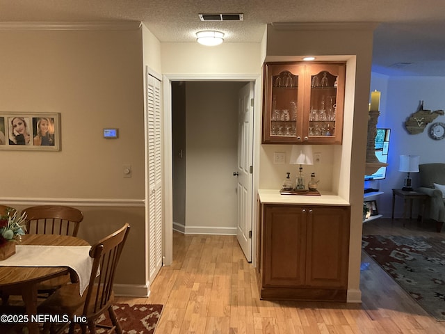 bar featuring crown molding, a textured ceiling, and light hardwood / wood-style flooring