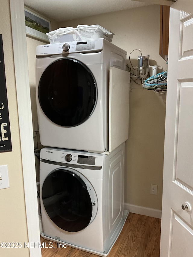 clothes washing area featuring stacked washer / drying machine and wood-type flooring