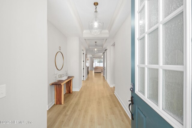 hall with a tray ceiling, baseboards, crown molding, and light wood finished floors