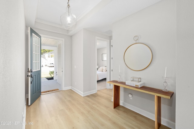 foyer entrance featuring a tray ceiling, crown molding, light wood-style flooring, and baseboards