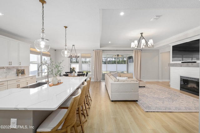 kitchen featuring light wood-style flooring, a large fireplace, a sink, white cabinets, and open floor plan