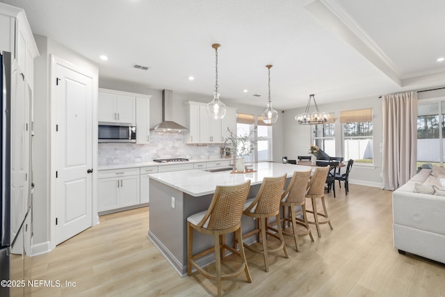 kitchen with appliances with stainless steel finishes, light wood-type flooring, wall chimney exhaust hood, and tasteful backsplash