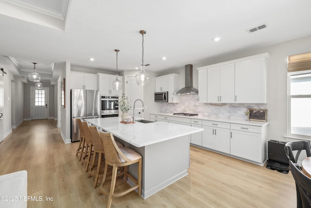 kitchen featuring stainless steel appliances, a sink, visible vents, decorative backsplash, and wall chimney exhaust hood