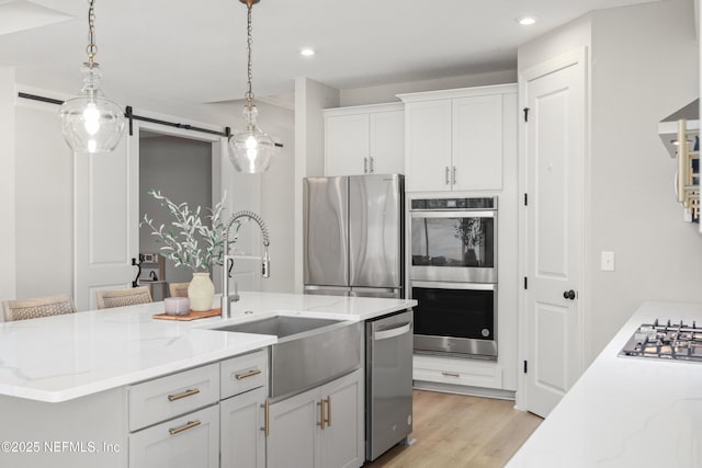 kitchen featuring light stone counters, stainless steel appliances, a sink, white cabinets, and light wood-style floors