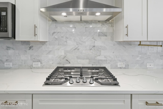 kitchen featuring light stone countertops, range hood, stainless steel appliances, white cabinetry, and backsplash