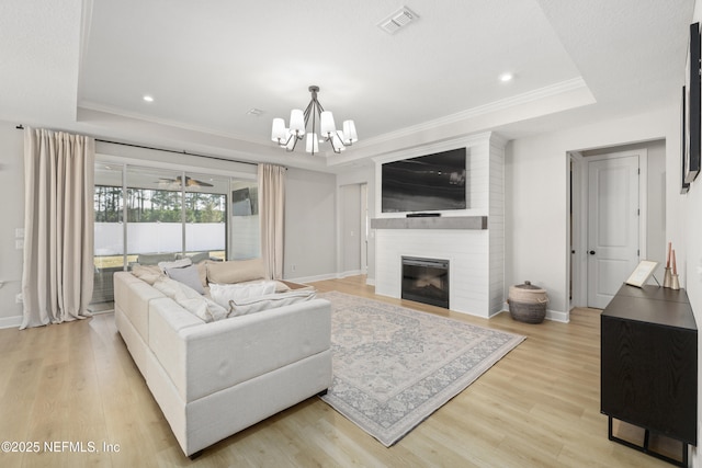 living room featuring light wood-type flooring, a fireplace, visible vents, and a raised ceiling