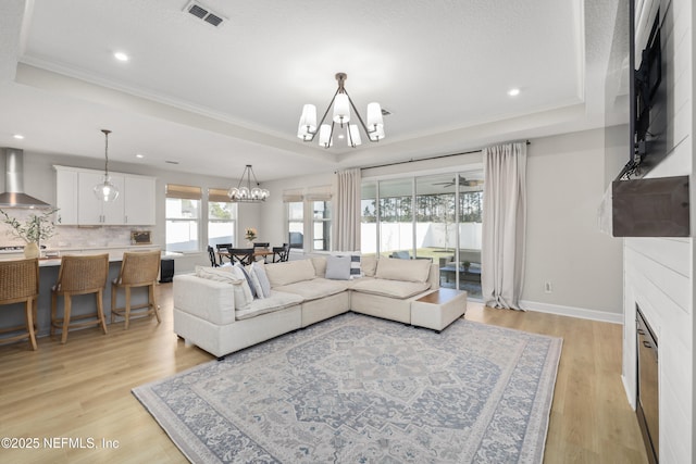 living area featuring a chandelier, a tray ceiling, light wood-style flooring, and visible vents