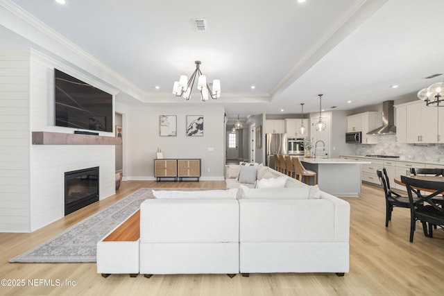 living room with light wood-style floors, crown molding, a tray ceiling, and a notable chandelier