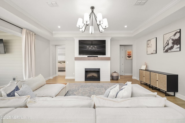 living area with a fireplace, visible vents, a raised ceiling, and wood finished floors