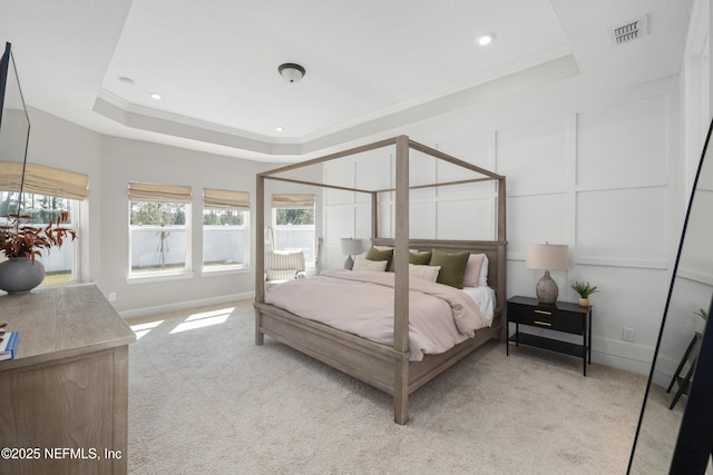 bedroom featuring a decorative wall, light colored carpet, visible vents, a tray ceiling, and crown molding