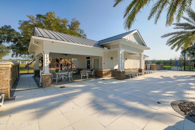 back of house featuring outdoor dining space, a standing seam roof, fence, and metal roof