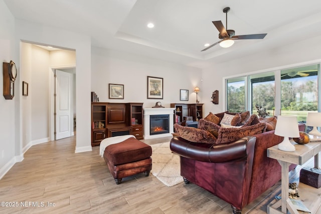 living room with ceiling fan, a raised ceiling, and light hardwood / wood-style flooring