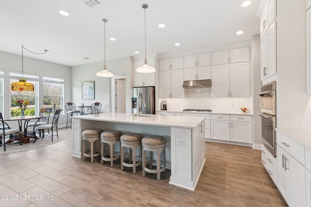 kitchen with appliances with stainless steel finishes, pendant lighting, white cabinetry, backsplash, and a center island with sink