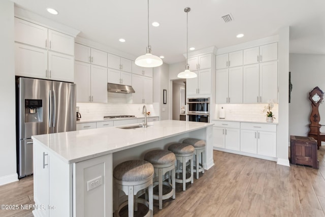 kitchen with decorative light fixtures, stainless steel appliances, an island with sink, and white cabinets