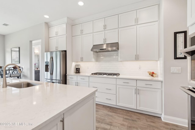 kitchen with sink, appliances with stainless steel finishes, white cabinetry, backsplash, and light stone countertops