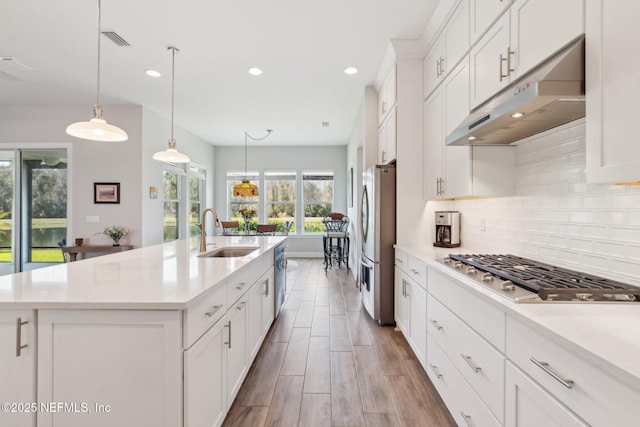 kitchen with appliances with stainless steel finishes, an island with sink, white cabinetry, sink, and hanging light fixtures