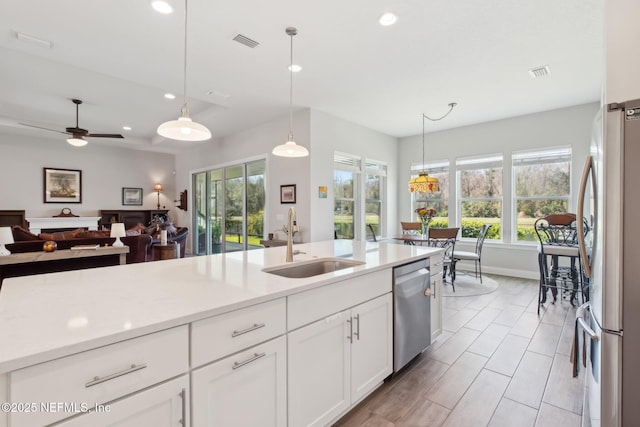 kitchen with pendant lighting, white cabinetry, sink, stainless steel appliances, and light stone countertops