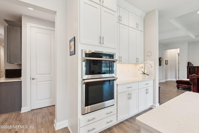 kitchen featuring white cabinets, stainless steel double oven, and light wood-type flooring