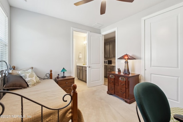 bedroom featuring ceiling fan, light colored carpet, and connected bathroom