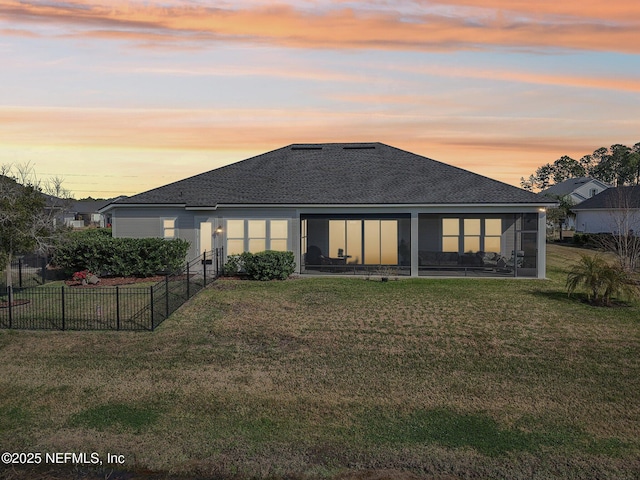 back house at dusk featuring a lawn and a sunroom