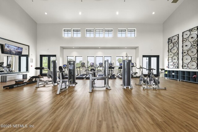 workout area featuring wood-type flooring, a towering ceiling, and french doors