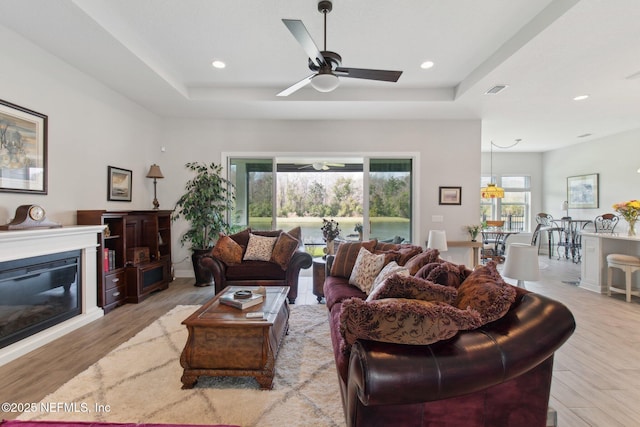 living room featuring ceiling fan, a tray ceiling, and light hardwood / wood-style flooring