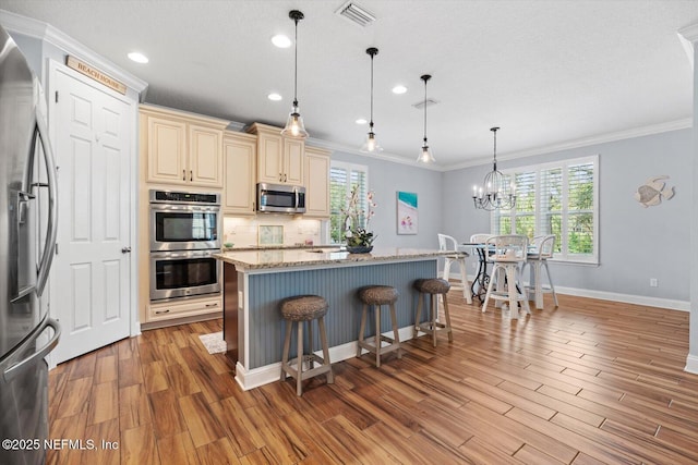 kitchen featuring light hardwood / wood-style flooring, appliances with stainless steel finishes, hanging light fixtures, light stone counters, and cream cabinets