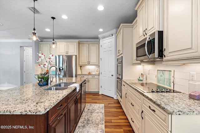 kitchen with pendant lighting, sink, stainless steel appliances, cream cabinets, and light stone countertops