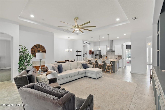 tiled living room with a raised ceiling and ceiling fan with notable chandelier