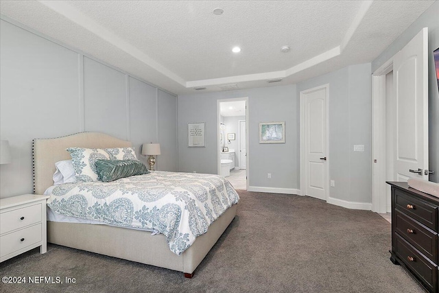 bedroom with a raised ceiling, ensuite bathroom, carpet flooring, and a textured ceiling