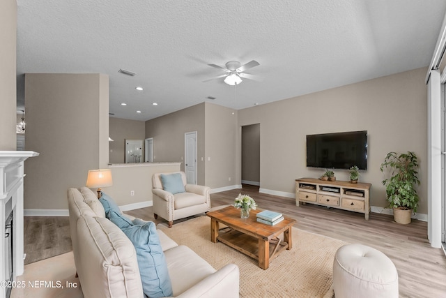 living room with ceiling fan, a textured ceiling, and light wood-type flooring