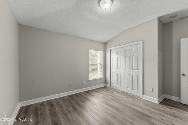 unfurnished bedroom featuring lofted ceiling, a textured ceiling, a closet, and light wood-type flooring