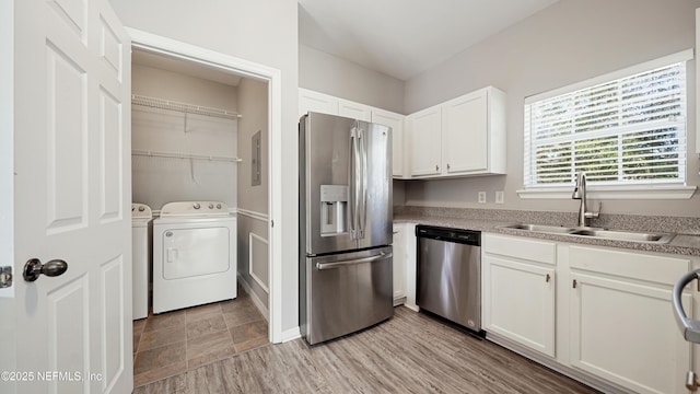 kitchen featuring appliances with stainless steel finishes, sink, white cabinets, light hardwood / wood-style floors, and washer and clothes dryer